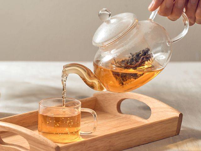 Tee aus einer Glaskanne wird in eine Glastasse eingegossen
