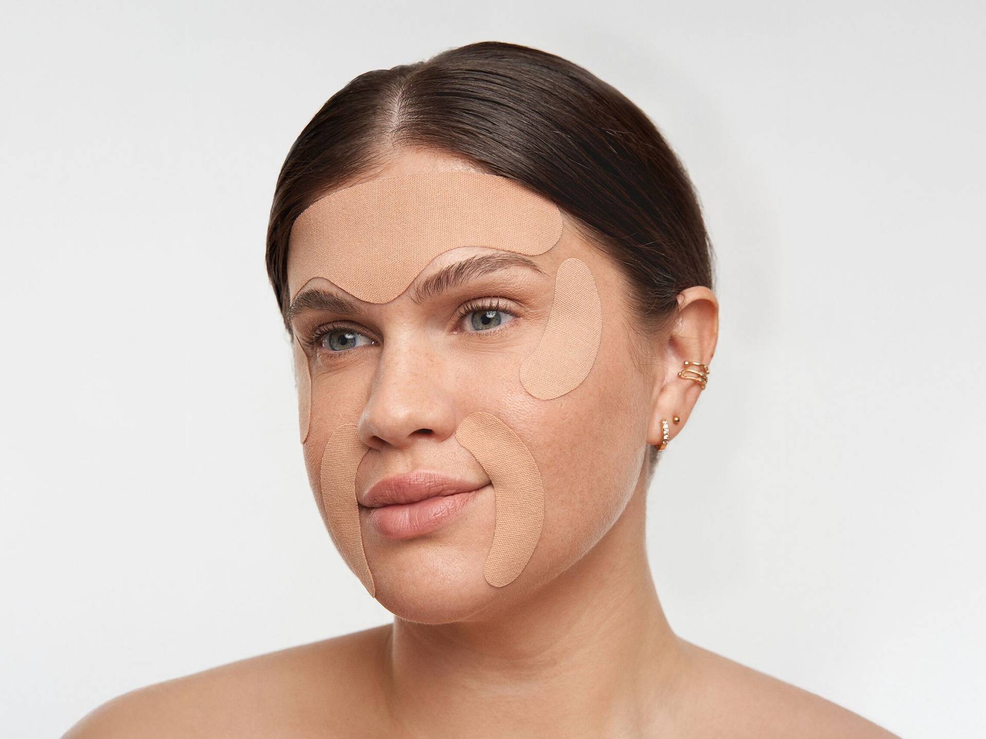 Frau mit glattem, zurückgekämmtem Haar und Skintapes im Gesicht angebracht