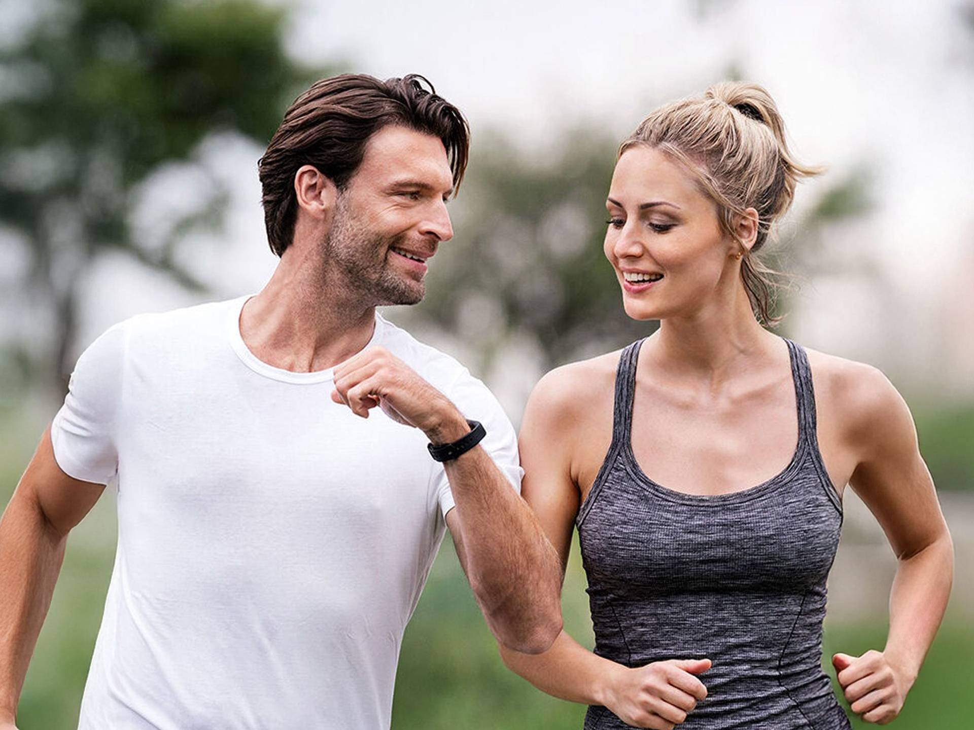 Ein junges Pärchen beim Joggen und er zeigt ihr die Daten auf seinem Fitnesstracker am Arm.