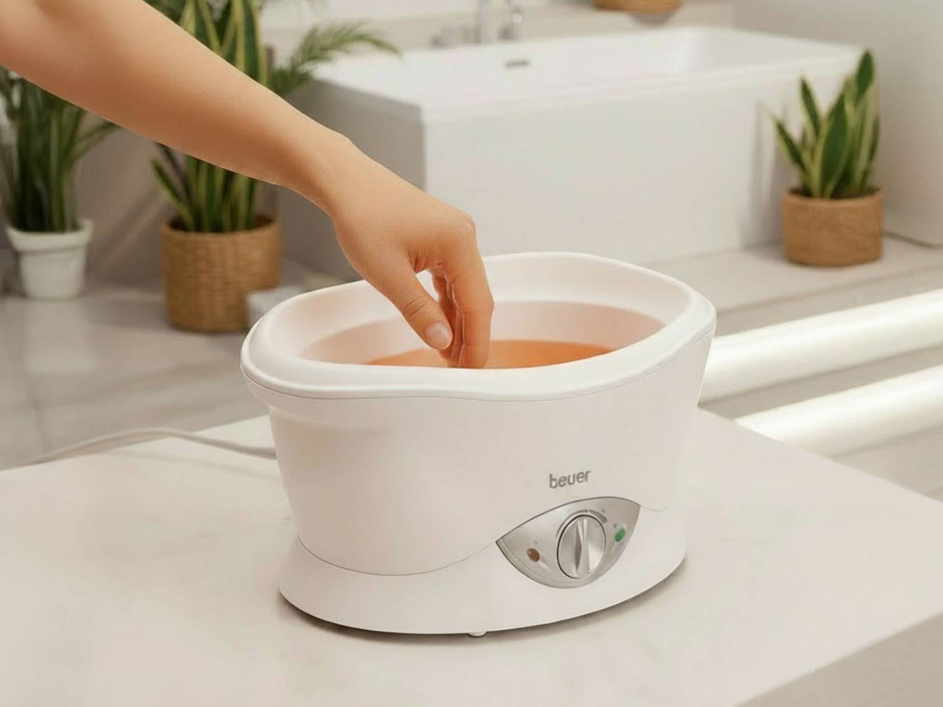 Hand taucht in weißes Beurer-Paraffinbad mit Temperaturregler und Kontrollleuchten ein