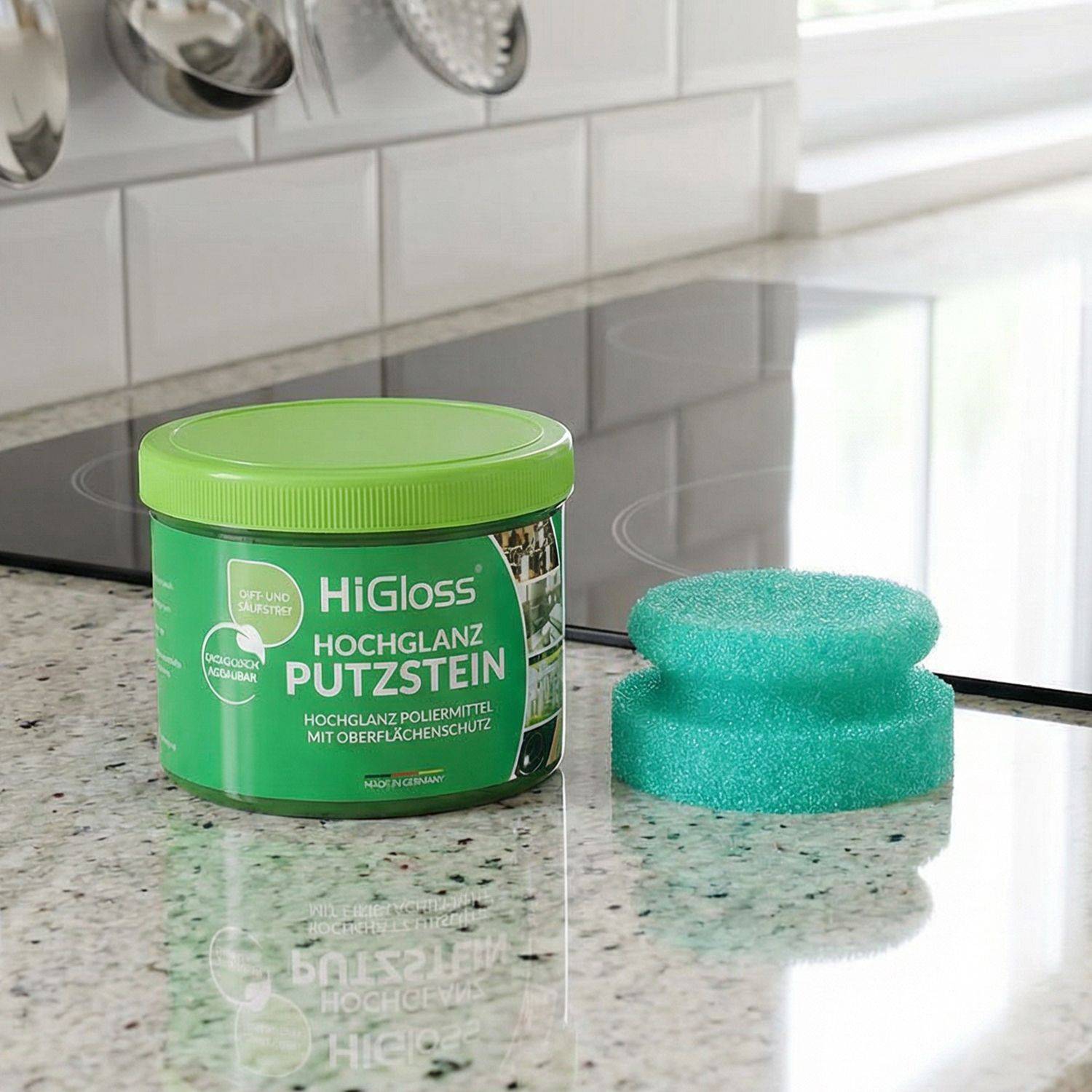 Grüner Behälter mit Aufschrift 'HiGloss Hochglanz Putzstein' neben grünem Schwamm auf Küchenarbeitsplatte vor Cerankochfeld