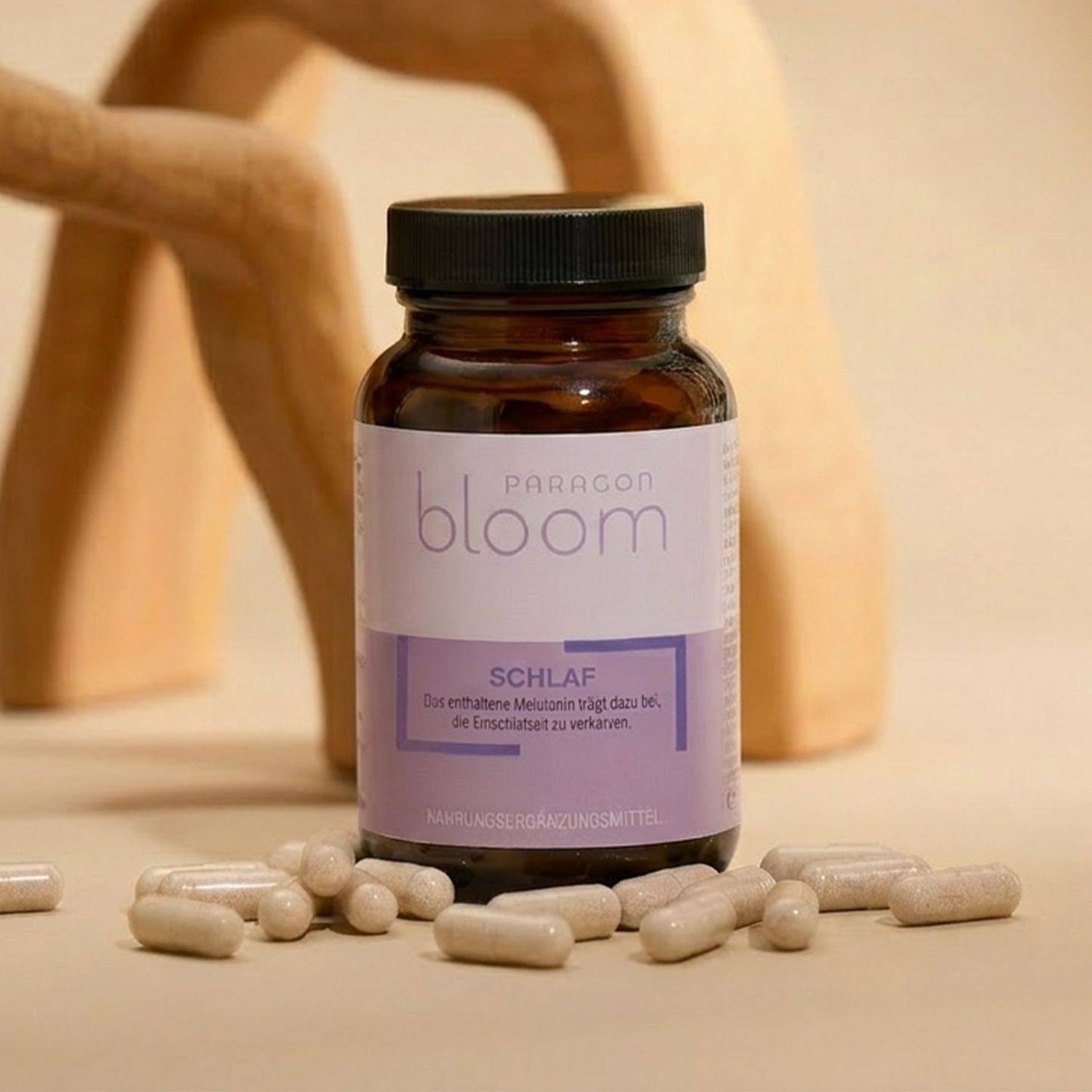 Braune Glasflasche mit schwarzem Deckel und lila Etikett mit der Aufschrift 'PARAGON bloom SCHLAF' umgeben von mehreren weißen Kapseln