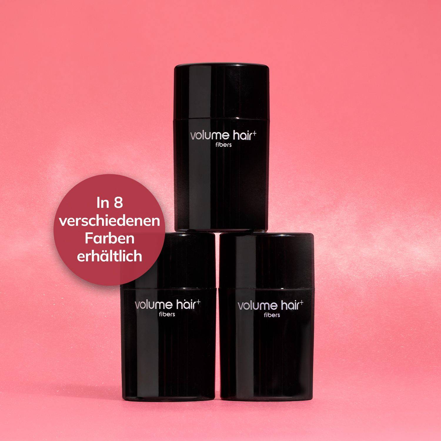 Drei schwarze Behälter mit der Aufschrift »volume hair fibers« vor rosa Hintergrund, daneben ein roter Kreis mit weißer Schrift »In 8 verschiedenen Farben erhältlich«