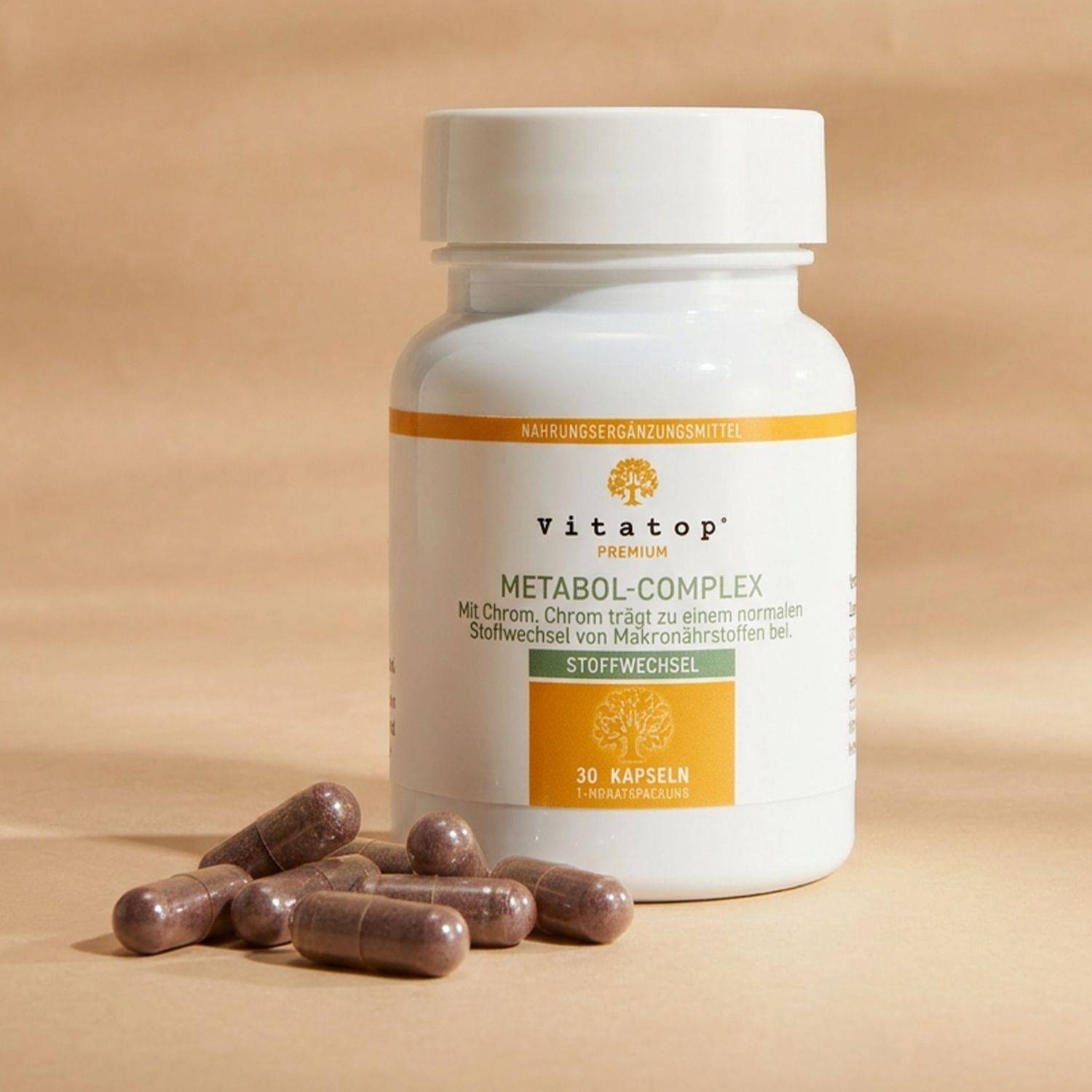 Weißer Kunststoffbehälter mit Etikett mit der Aufschrift 'Vitatop Metabol-Complex' sowie mehrere braune Kapseln davor