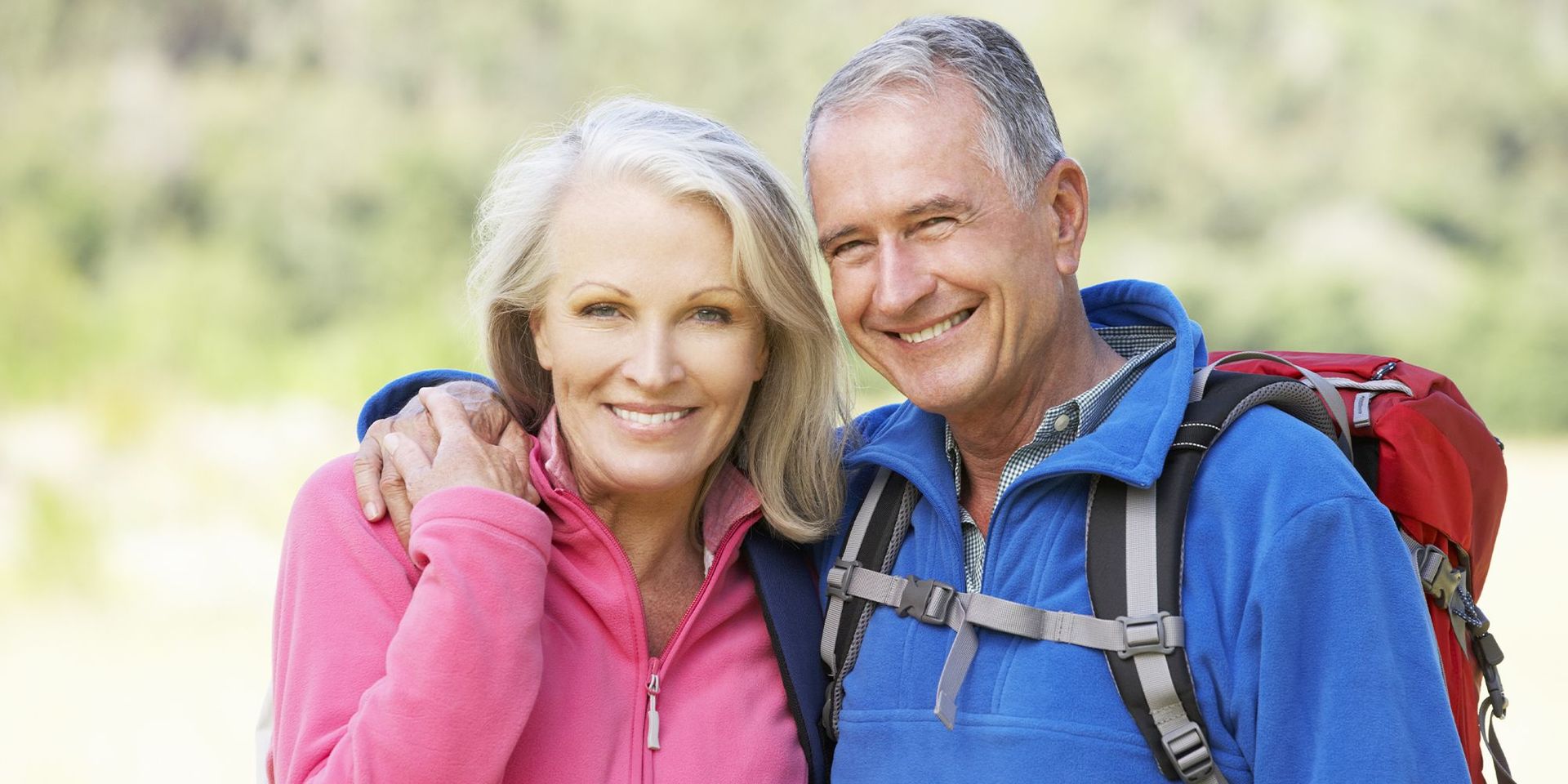 Älteres Paar in Outdoor-Kleidung lächelt in die Kamera, symbolisiert Mobilität und Wohlbefinden.