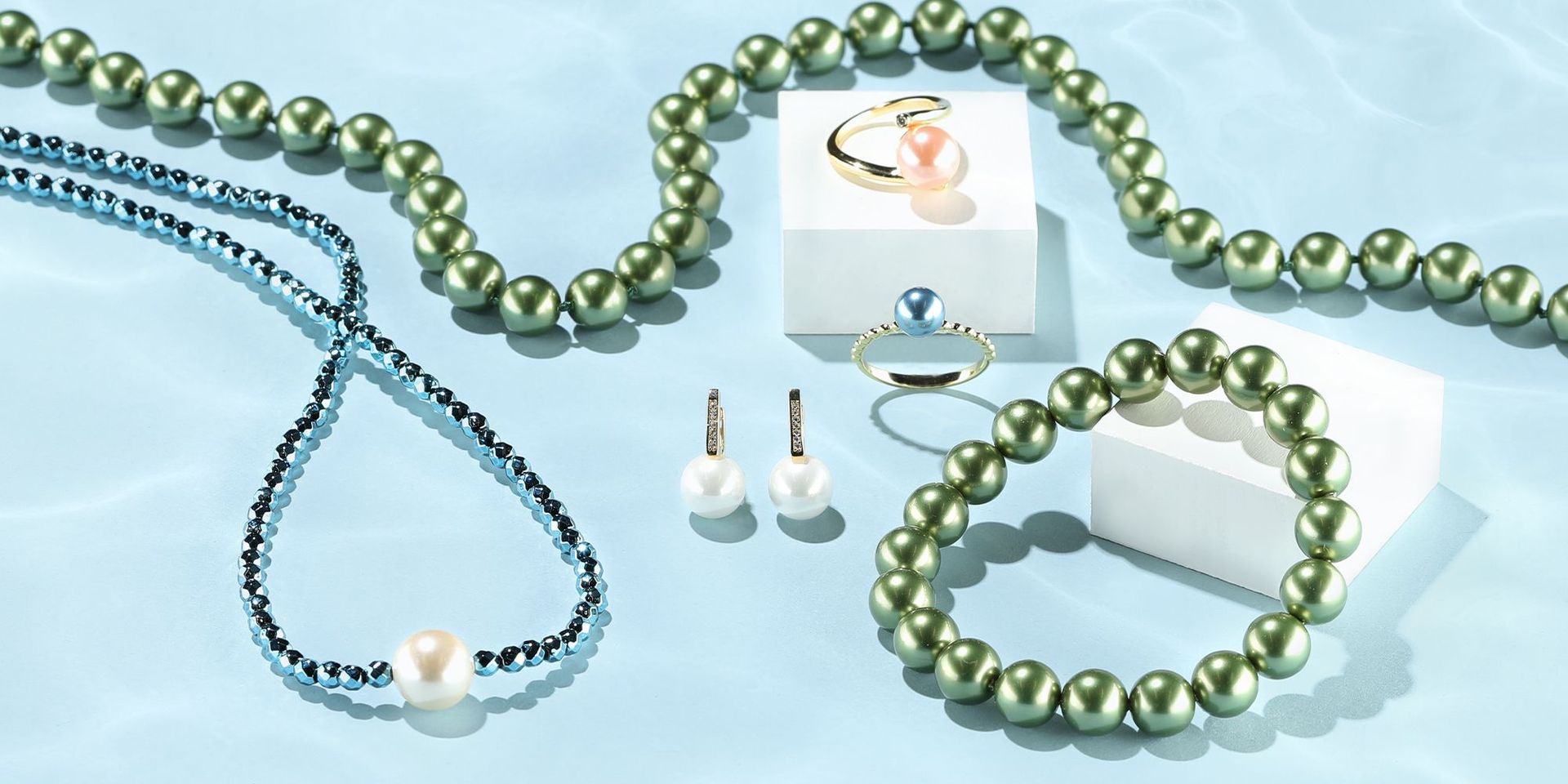 Grüne und blaue Perlenketten mit Ringen und Ohrringen auf hellem Hintergrund