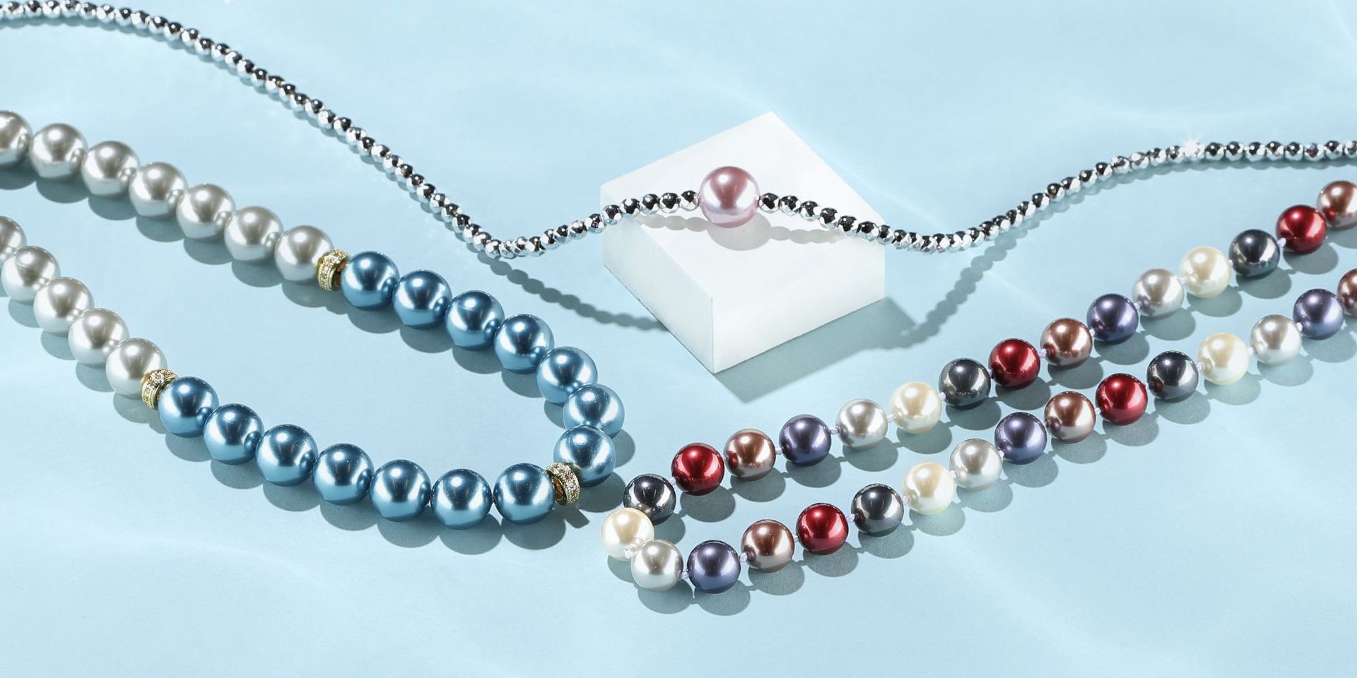 Perlenarmbänder in verschiedenen Farben auf hellblauem Hintergrund.