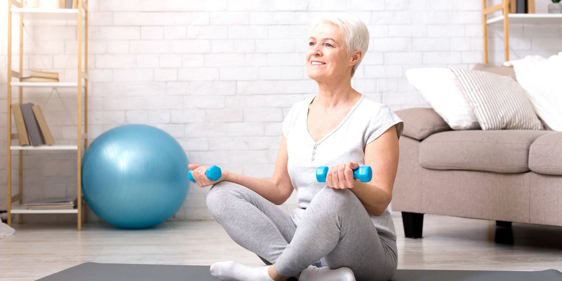 Ältere Frau beim Training mit Hanteln auf einer Yogamatte, Fokus auf Mobilität und Wohlbefinden.