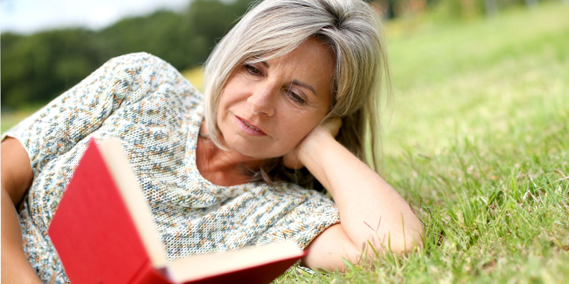 Frau liest entspannt ein Buch auf einer Wiese, symbolisiert Freizeit und Wohlbefinden.