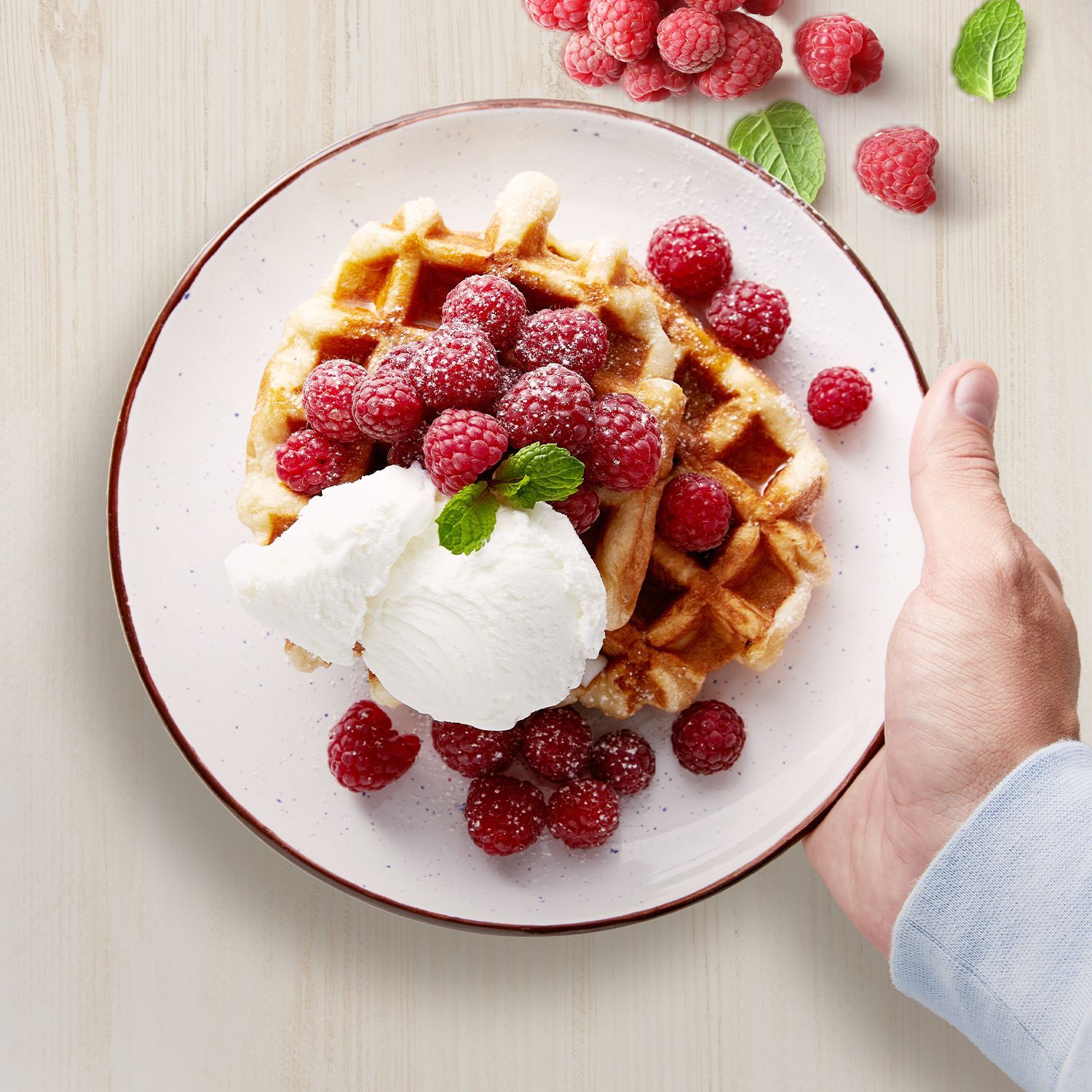 Waffeln mit Himbeeren und Sahne auf einem Teller, Hand hält den Teller