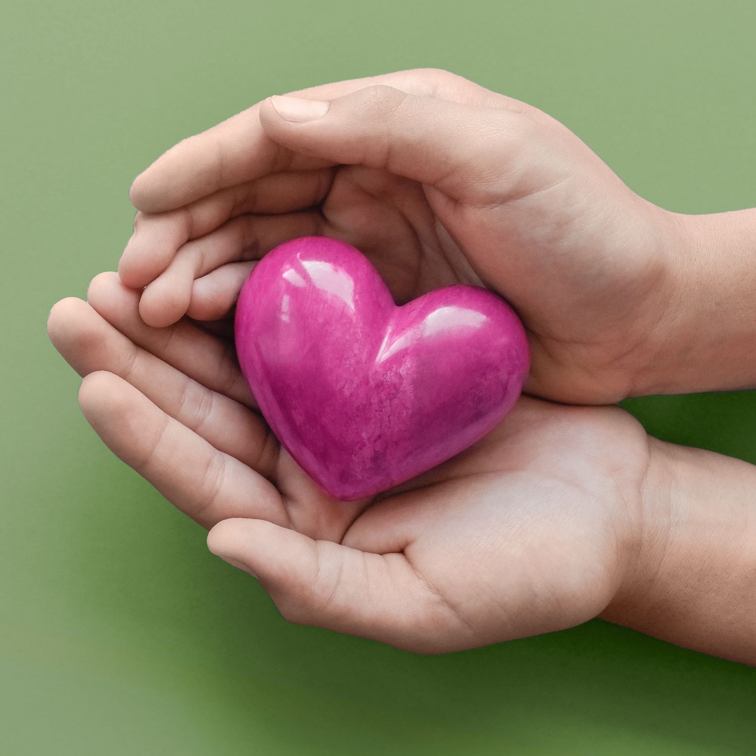Hände halten ein pinkes Herz vor grünem Hintergrund, symbolisiert Gesundheit und Fürsorge.
