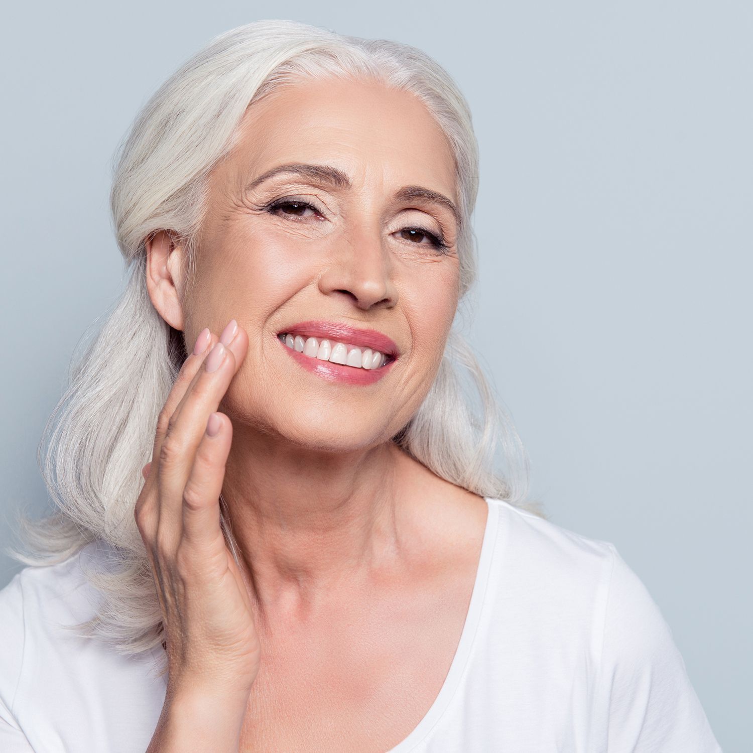 Lächelnde Frau mit grauen Haaren, streichelt leicht über ihr Gesicht