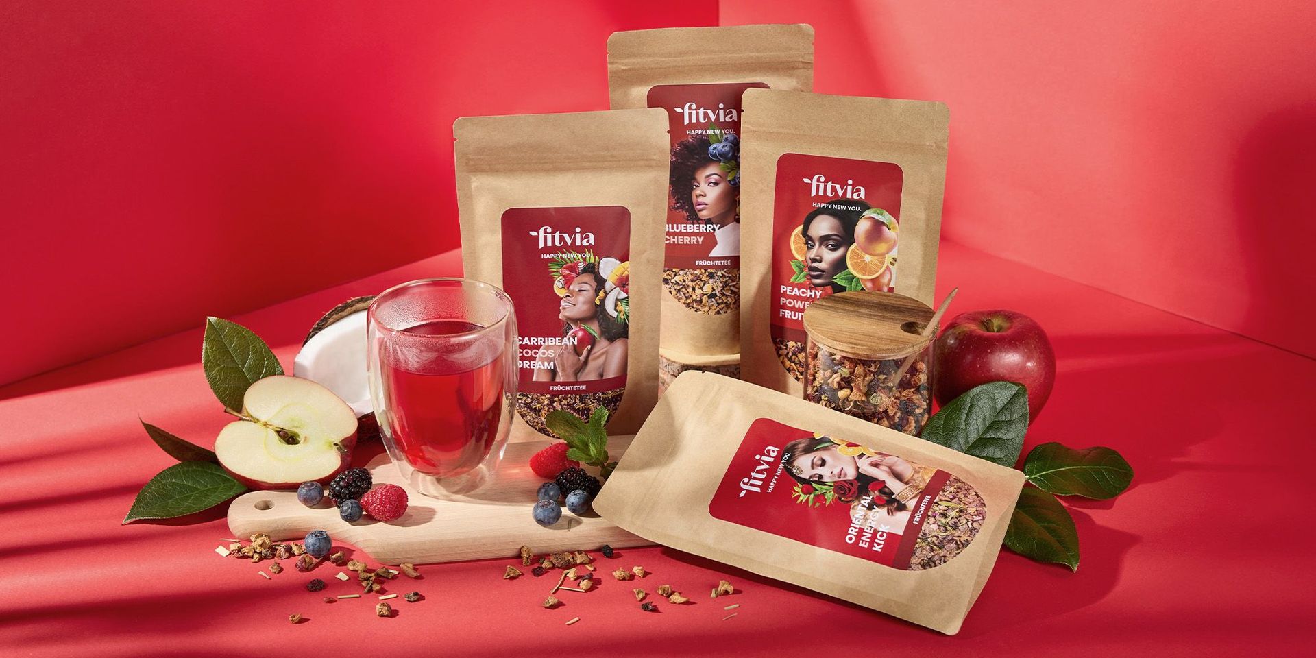 Fitvia Früchteteesortiment mit Beeren und Glas auf rotem Hintergrund
