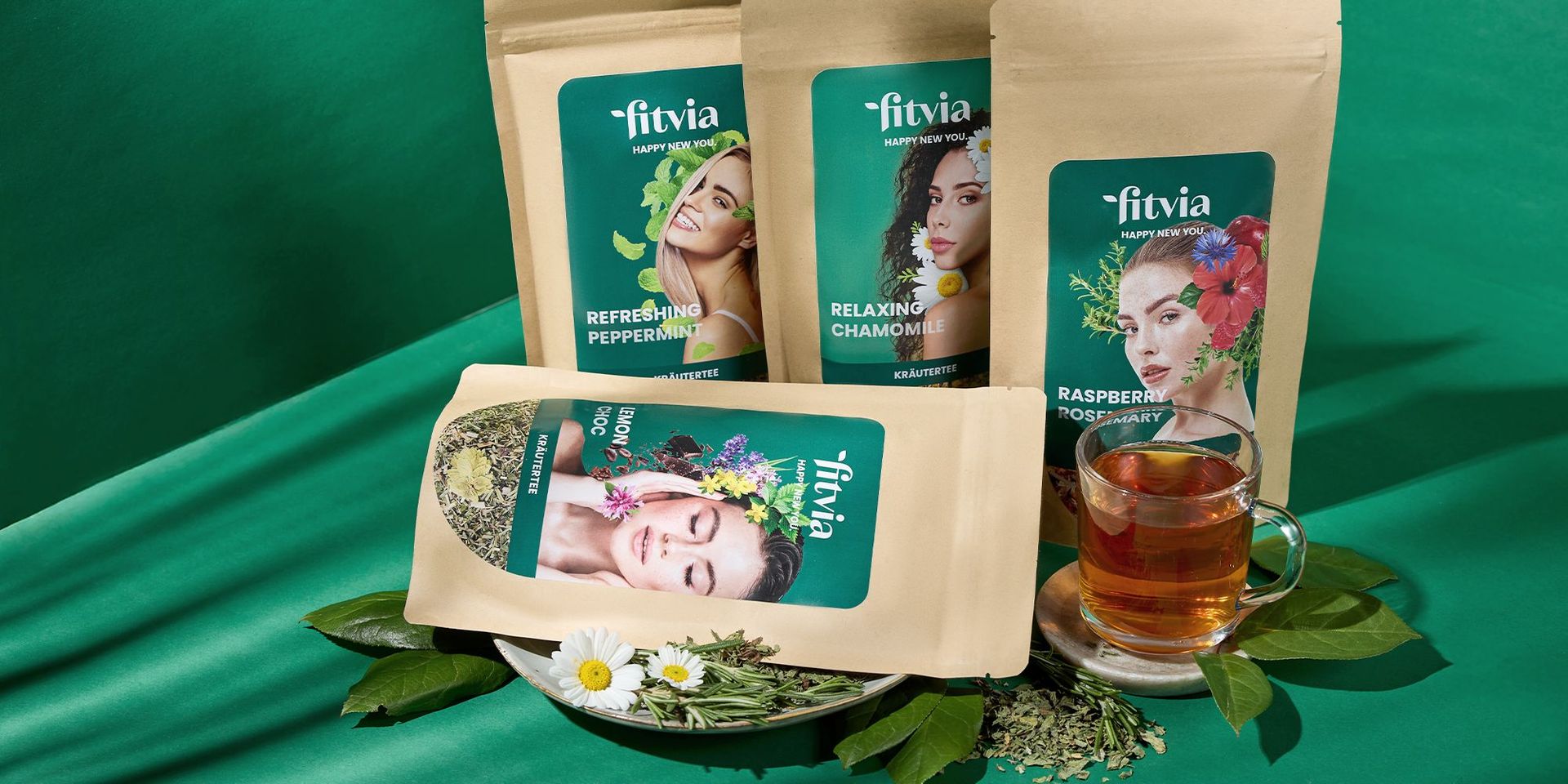 Fitvia Teesorten mit frischen Kräutern und Glas Tee, präsentiert auf grünem Hintergrund