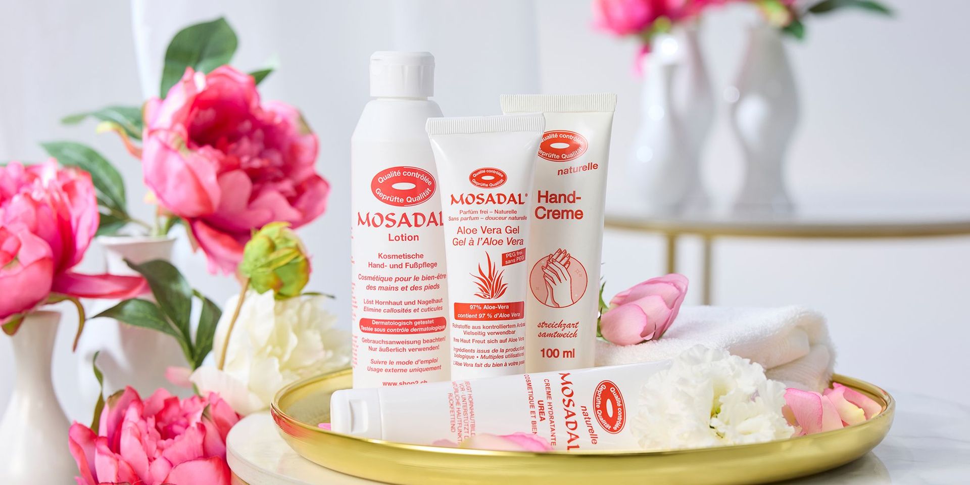 Ausgewählte Fußpflegeprodukte von Mosadal auf einem goldfarbenen Teller umgeben von pinken Pfingstrosen