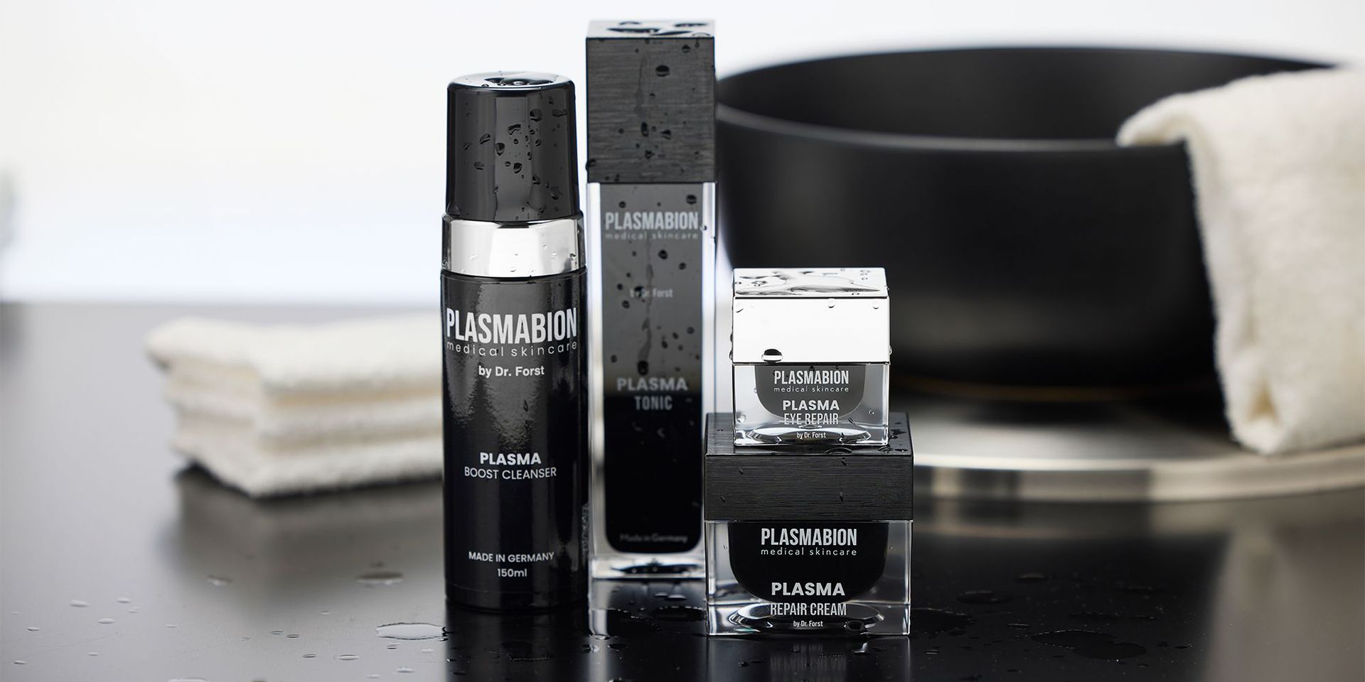 Ausgewählte Produkte von Plasmabion auf einem schwarzen Untergrund und einer schwarzen Schale und weißen Handtüchern im Hintergrund