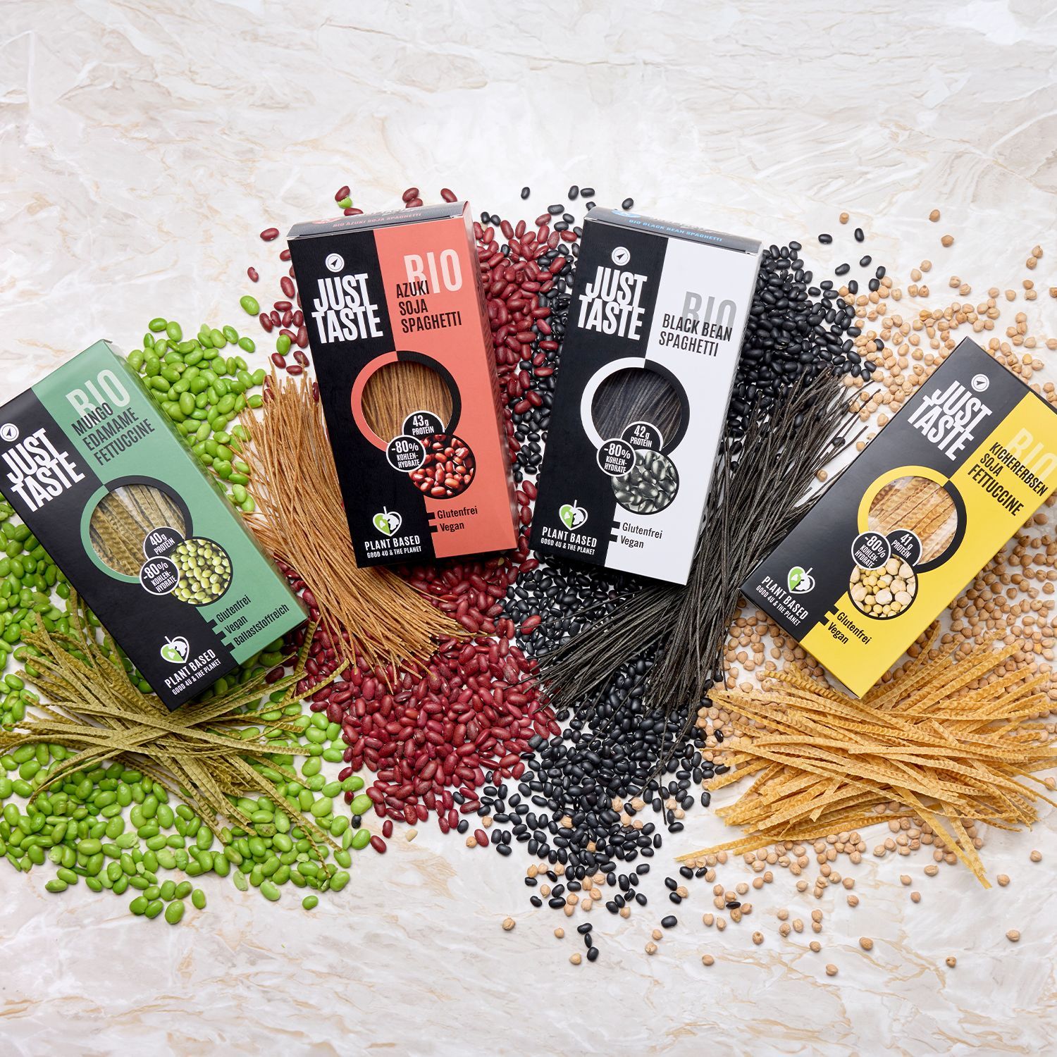 Vier Packungen Just Taste Bio-Spaghetti in verschiedenen Sorten mit passenden Hülsenfrüchten und Nudeln auf hellem Untergrund