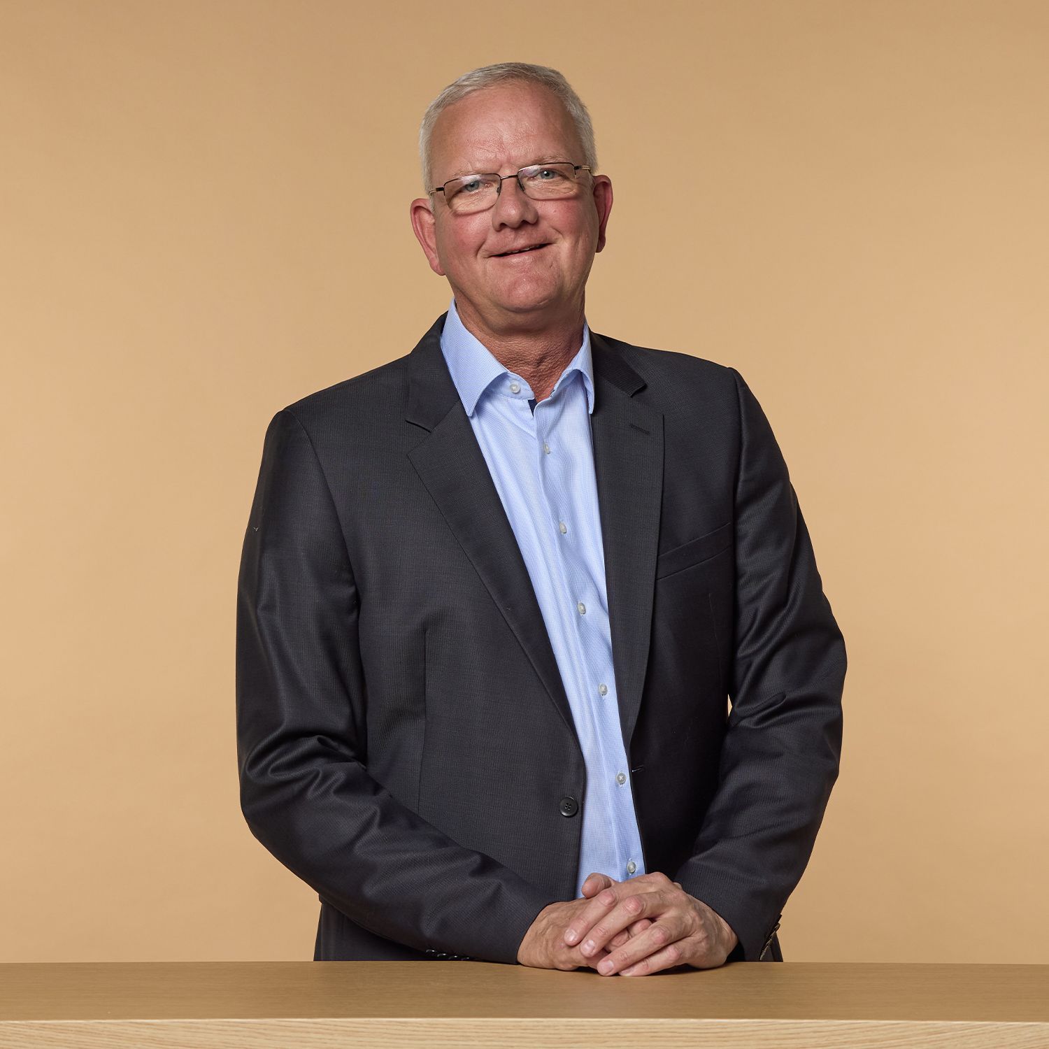 Vitatop-Experte Dr. med. Conrads trägt schwarzen Anzug und hellblaues Hemd, steht hinter einem Tisch mit verschränkten Händen.