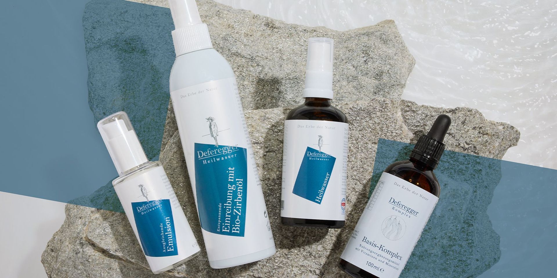 Vier Flaschen mit blauen Etiketten der Marke Deferegger Heilwasser, darunter Emulsion, Einreibung mit Bio-Zirbenöl, Heilwasser und Basis-Komplex, auf Steinuntergrund.