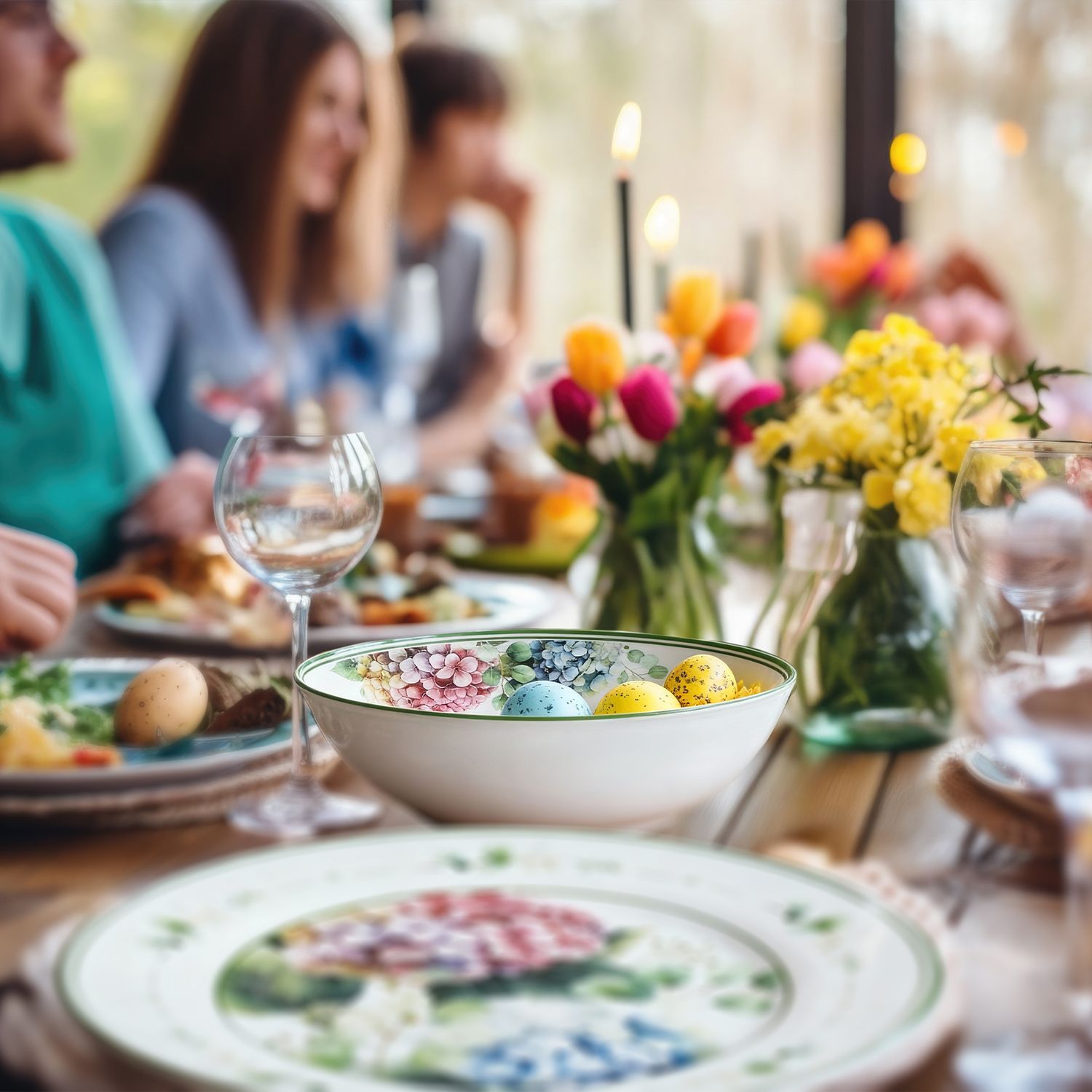 Ostertisch mit bunten Eiern in einer Schale, Blumenvasen und mehreren Personen im Hintergrund