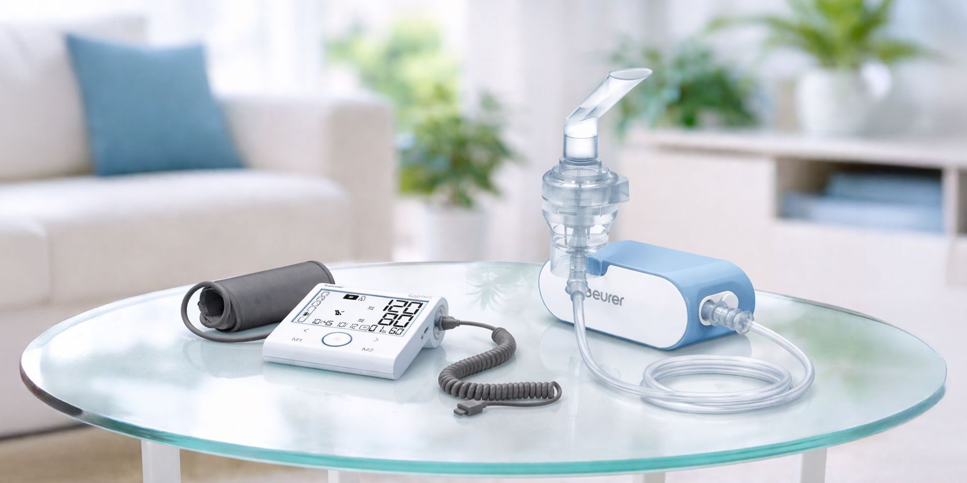 Blau-weißes Inhalationsgerät und digitales Blutdruckmessgerät mit Manschette auf einem Glastisch in einem hellen Raum