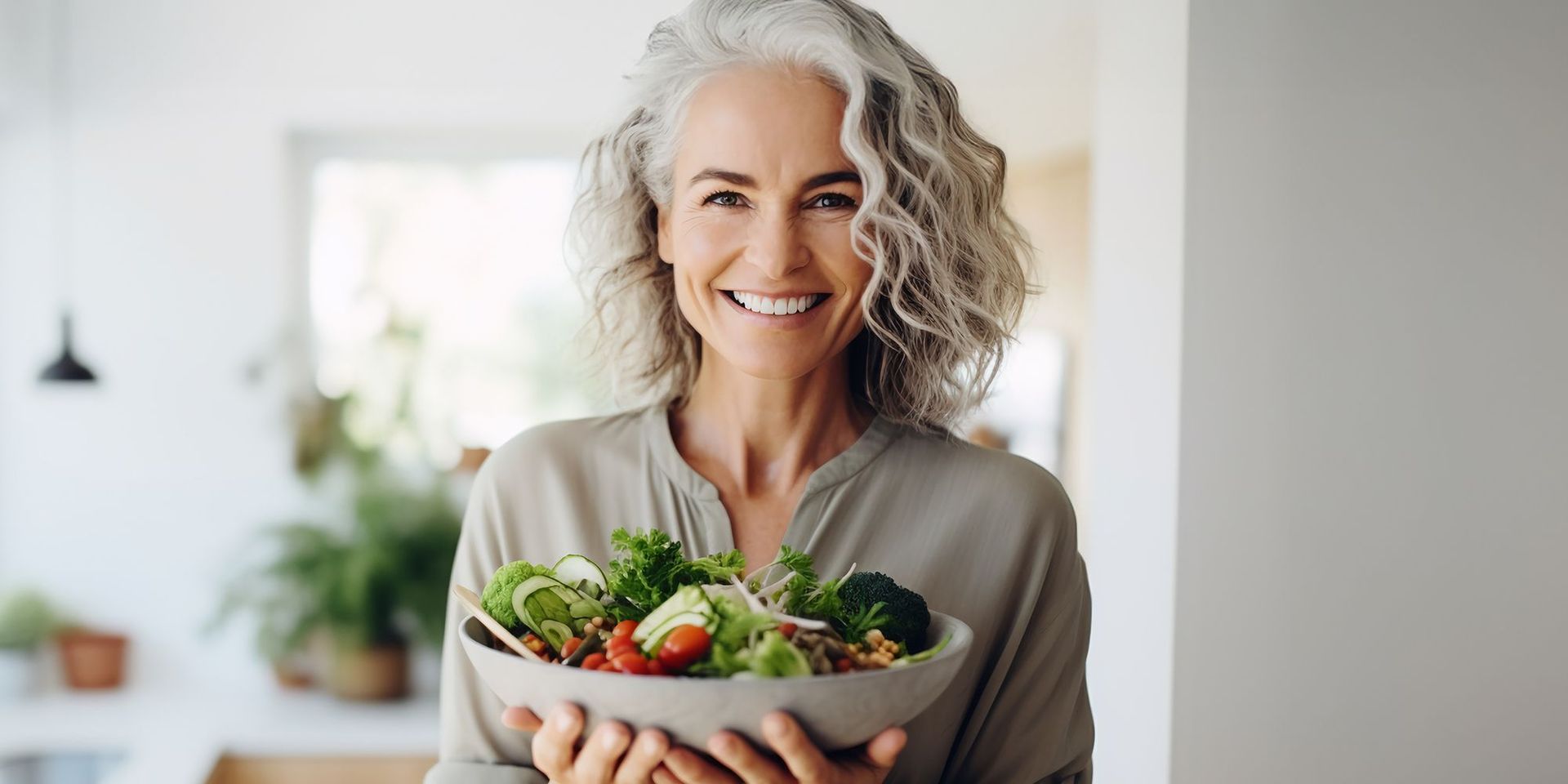 Frau mit grauen lockigen Haaren hält eine Schüssel mit frischem Salat und lächelt