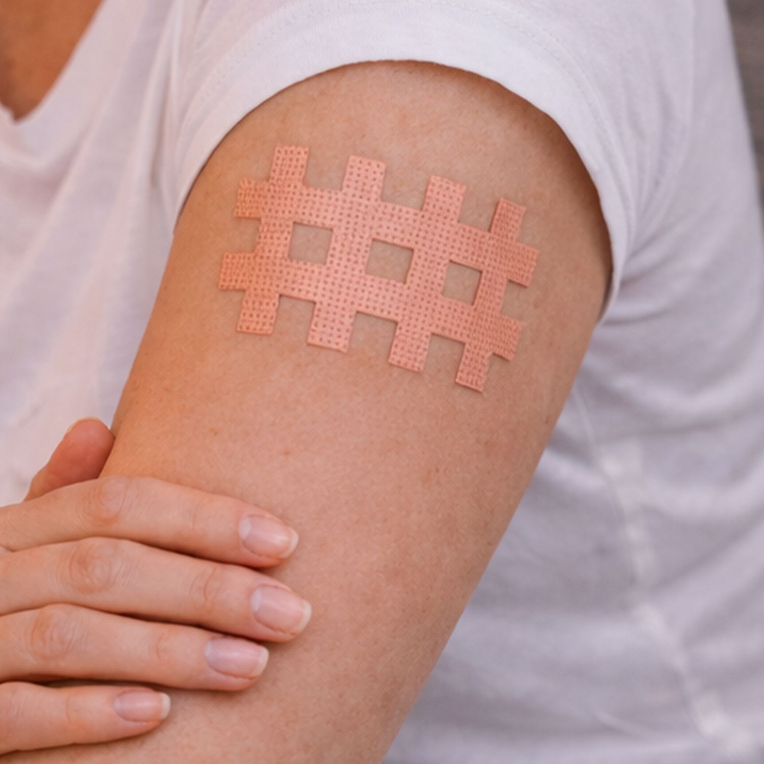 Oberarm mit Akupunkturpflaster in Gitterform und Hand, die den Arm hält