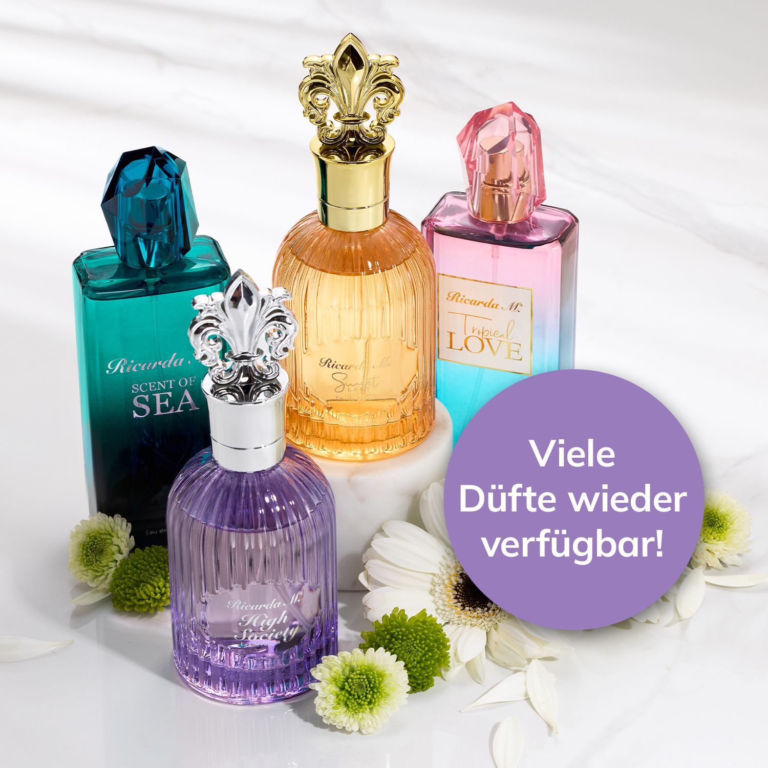 Vier unterschiedlich geformte und farbige Parfümflakons mit verzierten Verschlüssen stehen neben weißen und grünen Blumen auf weißem Untergrund