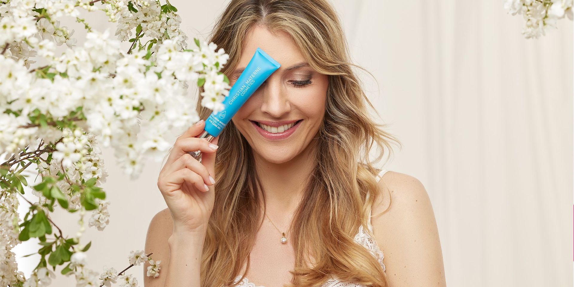 Frau mit langen, gewellten Haaren hält ein kleines blaues Fläschchen neben weißen Blüten