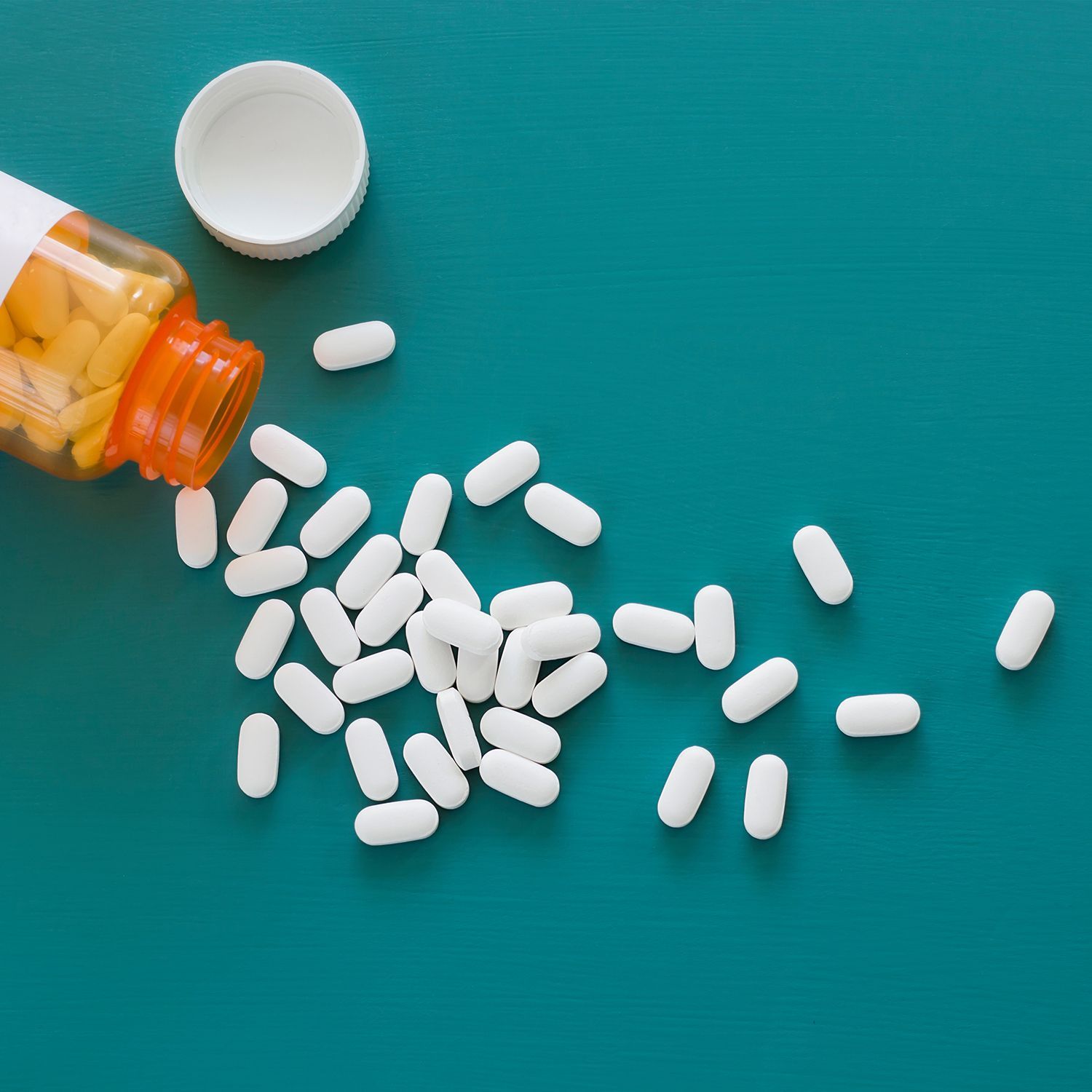 Zu den Nahrungsergänzungsmitteln Eine offene Pillendose aus der weiße Pillen fallen vor einem grün-blauen Hintergrund.