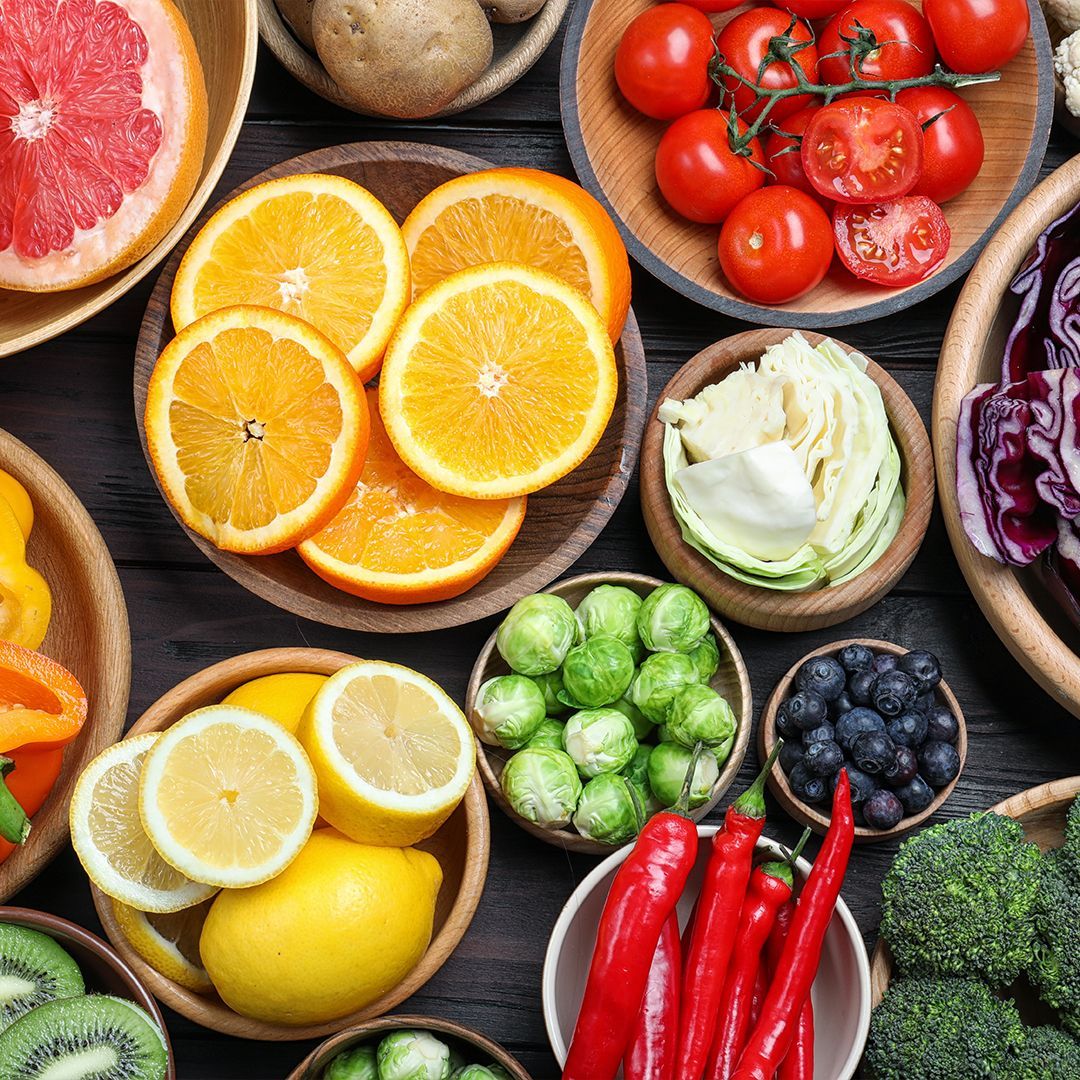 Vitamin C Verschiedene Obst- und Gemüsesorten in Schalen und auf einem dunklen Untergrund, darunter Orangen-, Grapefruit- und Zitronenscheiben, Rosenkohl, Kirschtomaten, Heidelbeeren sowie Rot- und Weißkohl