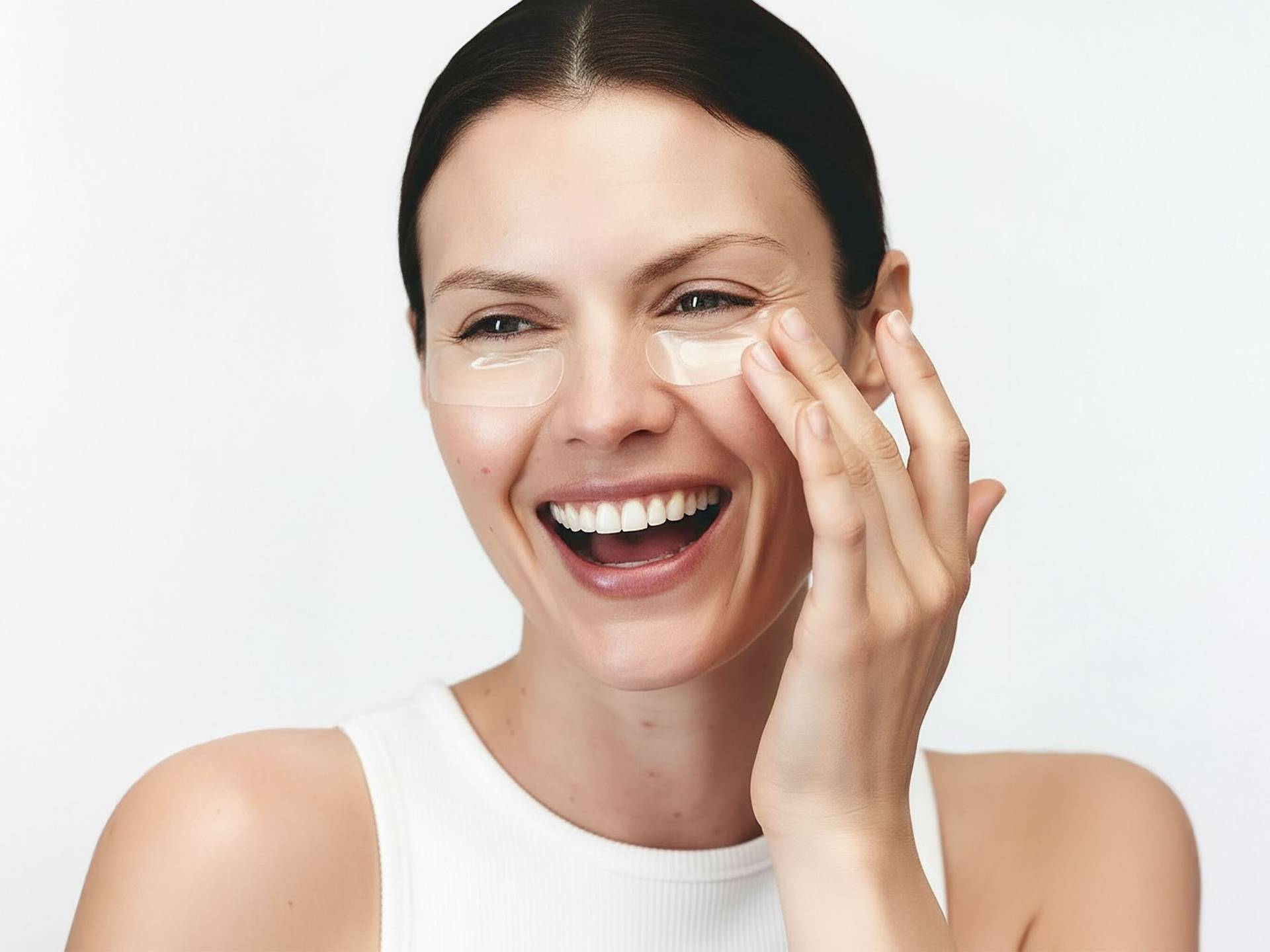 Microneedling Patches – nadelfreie Anti-Aging-Innovation mit Botulin-Komplex Frau mit zurückgebundenem Haar trägt natürliche Botulin-Microneedling-Patches unter den Augen, trägt weißes ärmelloses Oberteil.