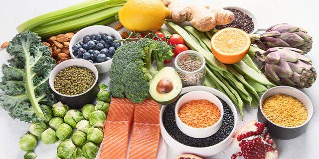 Gesunde Lebensmittel Verschiedene gesunde Lebensmittel wie Brokkoli, Avocado, Linsen, Lachs, Artischocke, Blaubeeren, Orangen und Grünkohl auf weißem Untergrund arrangiert