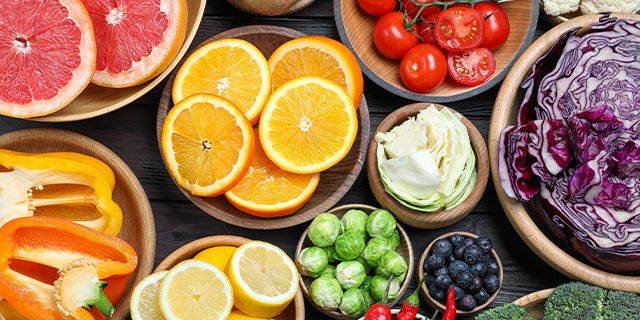 Vitamin C in Obst und Gemüse Nahaufnahme von halbierten Orangen, einer halbierten Zitrone, Rosenkohl, Heidelbeeren, geschnittenem Weißkohl und Rotkohl in Schalen und auf einem Holzbrett