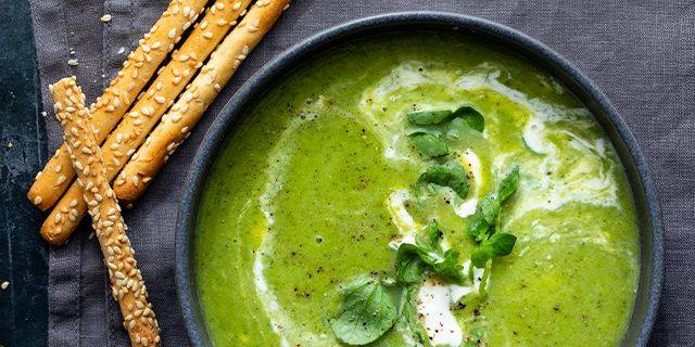 Suppe mit Brunnenkresse Schale mit grüner Suppe, garniert mit Brunnenkresse, daneben Sesamstangen auf dunklem Stoff