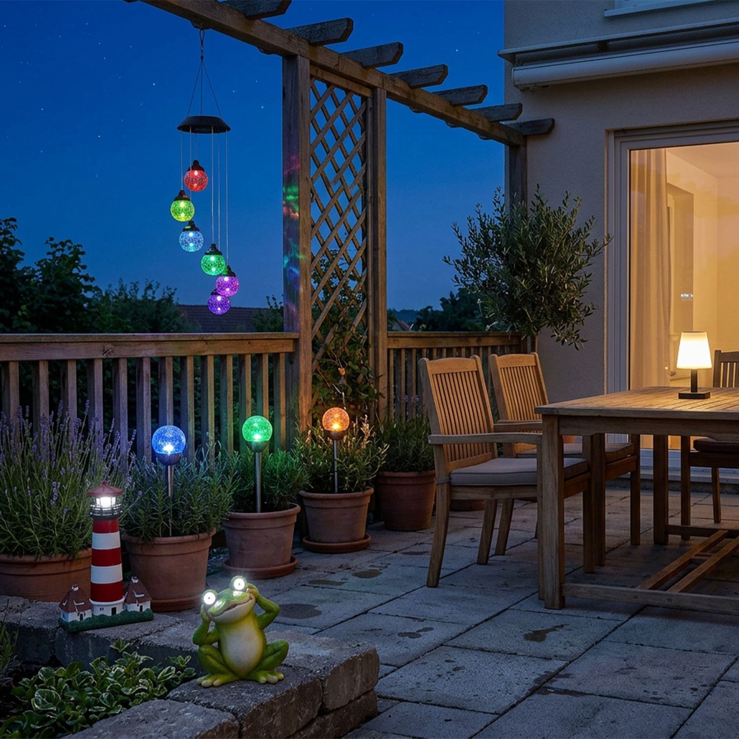 Warmes Licht für Ihren Garten Terrasse mit Holztisch und Stühlen, beleuchteten bunten Kugeln an einer Pergola, einem kleinen Leuchtturm und einer Froschfigur mit Licht