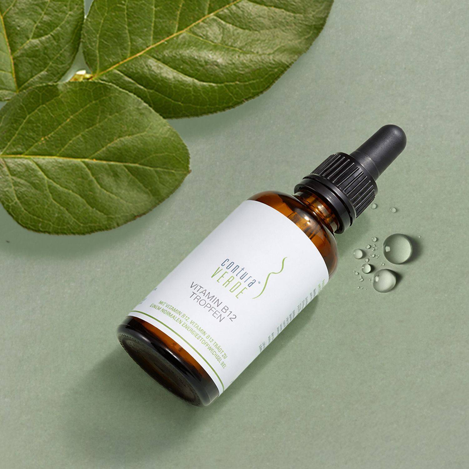 Hochwertiges Vitamin B12 – Vitamin B12 Tropfen von Contura Verde Braune Glasflasche mit Pipette und weißem Etikett mit Aufschrift 'Contura Verde Vitamin B12 Tropfen' liegt neben grünen Blättern und Tropfen auf grünem Untergrund